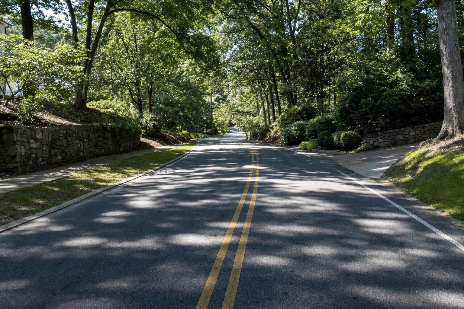 Calle residencial de dos carriles en Sandy Springs, Georgia, a plena luz del día, con banquetas interrumpidas, árboles junto al hombro y una entrada de casa que reduce la visibilidad del conductor.